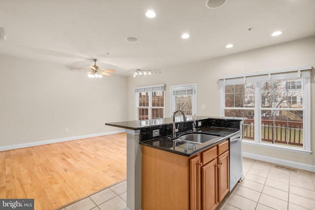 kitchen with sink, dishwasher, ceiling fan, a kitchen island with sink, and dark stone countertops