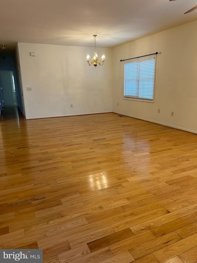 spare room featuring a chandelier and light hardwood / wood-style floors