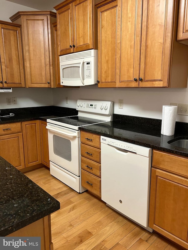 kitchen featuring white appliances, dark stone counters, sink, and light hardwood / wood-style floors