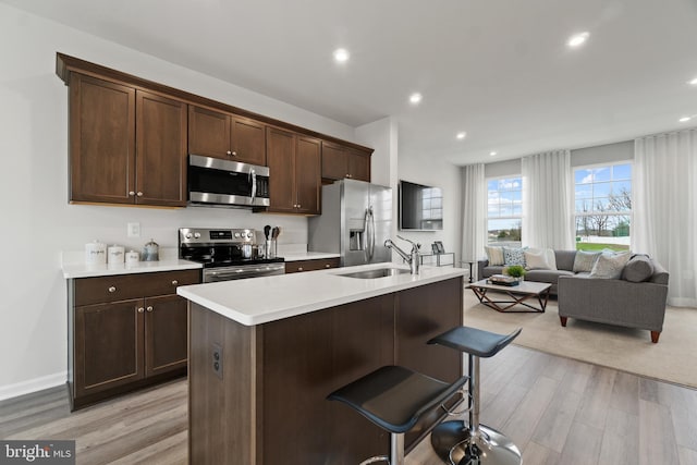 kitchen featuring a center island with sink, light countertops, appliances with stainless steel finishes, open floor plan, and a sink