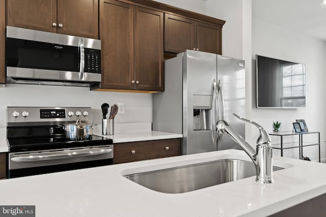 kitchen with stainless steel appliances, light countertops, a sink, and dark brown cabinets