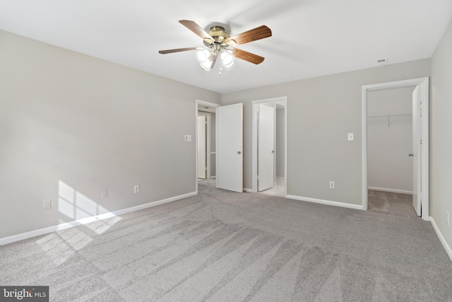 unfurnished bedroom featuring ceiling fan, a closet, a spacious closet, and light carpet