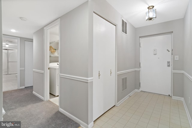 foyer entrance with washer / dryer and light carpet