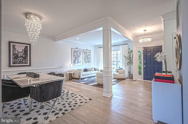 foyer entrance featuring decorative columns, crown molding, a chandelier, and light wood-type flooring