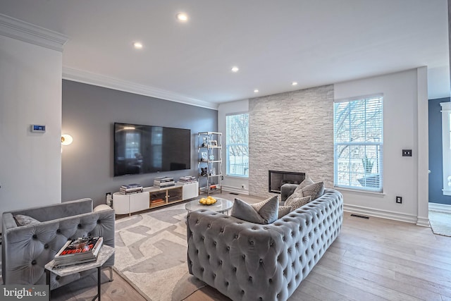 living room with crown molding, a stone fireplace, a healthy amount of sunlight, and light wood-type flooring