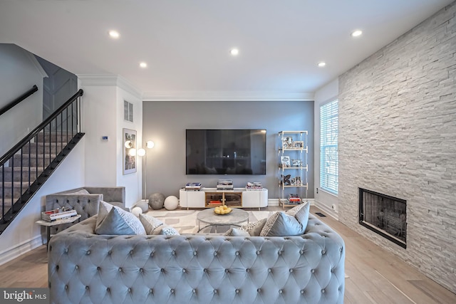 living room featuring ornamental molding, a stone fireplace, and light hardwood / wood-style floors