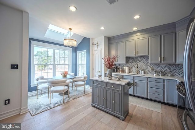 kitchen featuring sink, light hardwood / wood-style flooring, gray cabinetry, decorative light fixtures, and vaulted ceiling