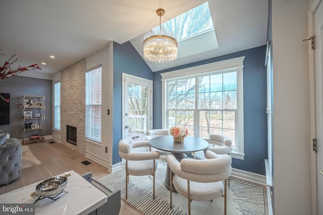 dining area featuring vaulted ceiling, a chandelier, a fireplace, and light hardwood / wood-style flooring