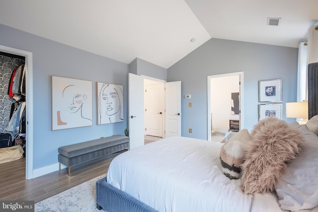 bedroom with lofted ceiling, a walk in closet, dark wood-type flooring, ensuite bath, and a closet