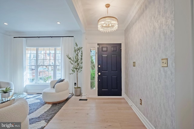 foyer entrance with ornamental molding, an inviting chandelier, and light hardwood / wood-style floors