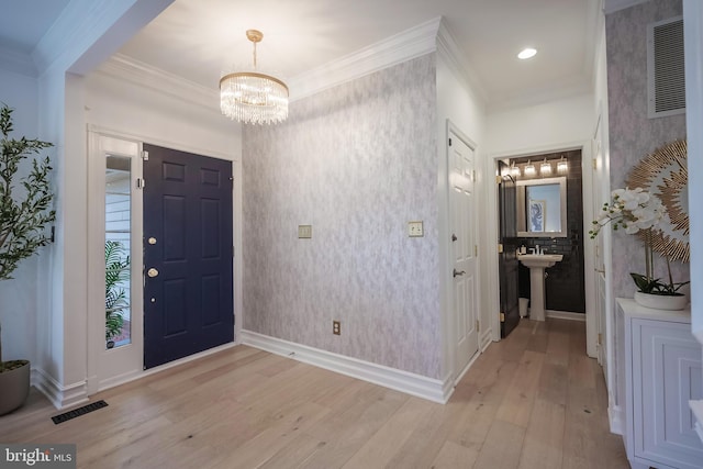 foyer entrance with crown molding, sink, an inviting chandelier, and light wood-type flooring