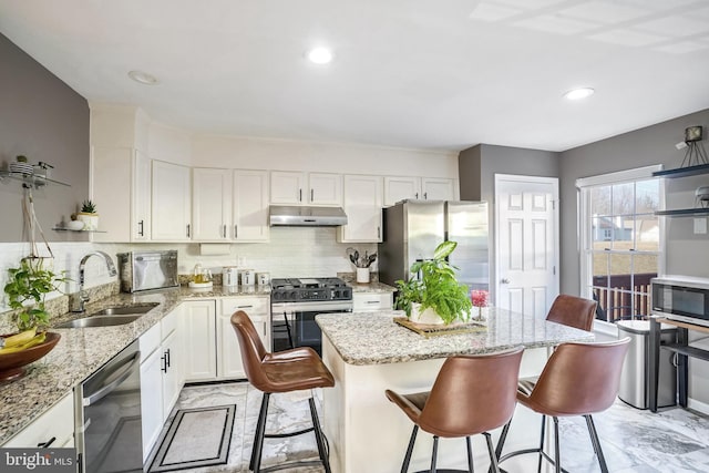 kitchen with appliances with stainless steel finishes, a breakfast bar, sink, and light stone countertops