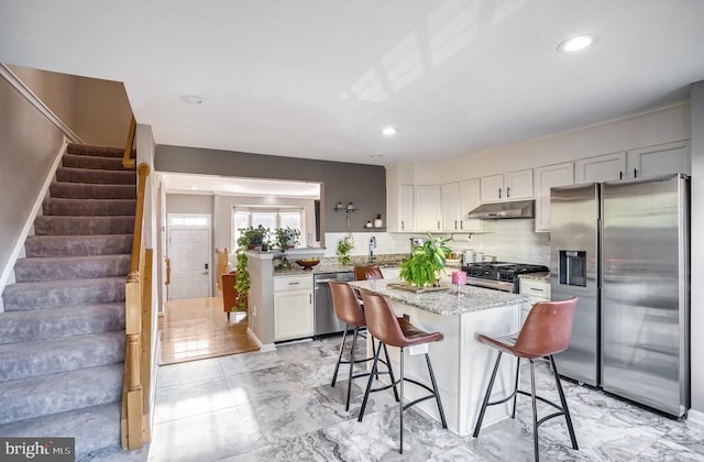 kitchen featuring appliances with stainless steel finishes, a kitchen breakfast bar, light stone counters, white cabinets, and decorative backsplash