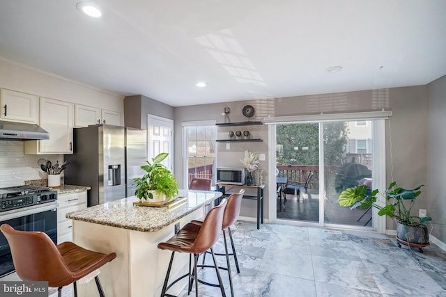 kitchen featuring a kitchen island, a breakfast bar, white cabinetry, light stone counters, and stainless steel appliances