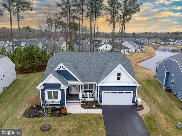 view of front of property featuring a garage, a water view, covered porch, and a lawn