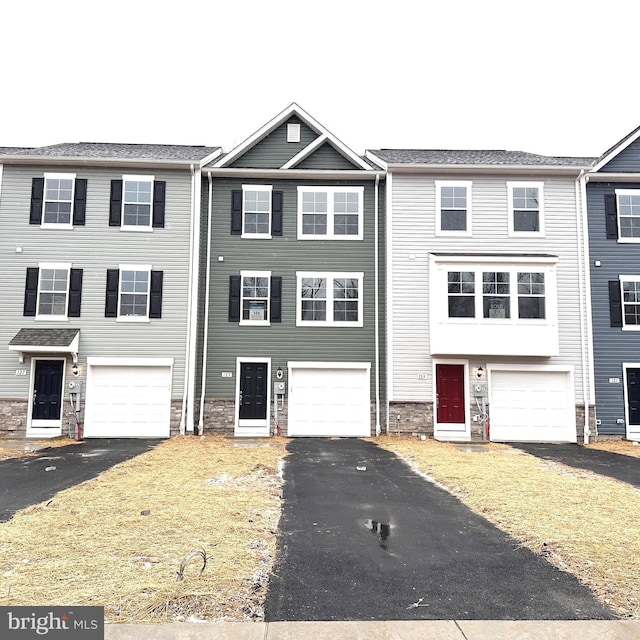 townhome / multi-family property with a garage, driveway, and stone siding