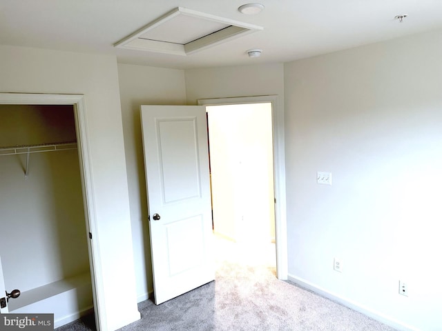 unfurnished bedroom with a closet, carpet flooring, attic access, and baseboards