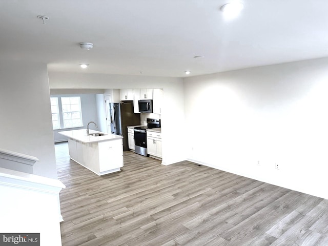 kitchen featuring stainless steel appliances, light countertops, an island with sink, and white cabinetry