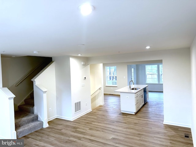 kitchen featuring light wood finished floors, light countertops, visible vents, an island with sink, and dishwasher