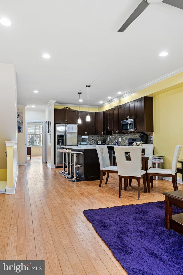 kitchen with dark brown cabinetry, a breakfast bar area, hanging light fixtures, light hardwood / wood-style flooring, and stainless steel appliances