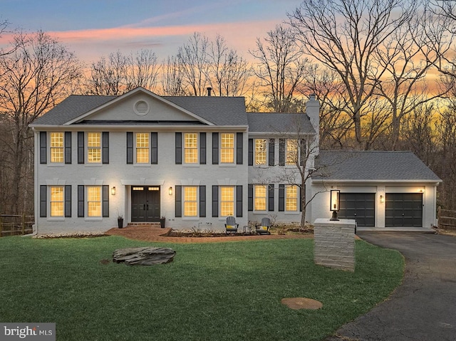 view of front facade featuring a front lawn, aphalt driveway, an attached garage, brick siding, and a chimney