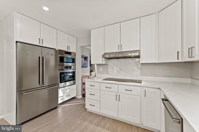 kitchen with light wood-style floors, appliances with stainless steel finishes, light stone counters, under cabinet range hood, and white cabinetry