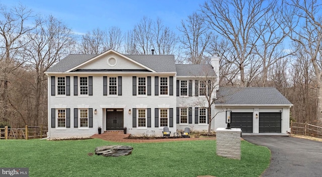 colonial-style house featuring aphalt driveway, brick siding, an attached garage, fence, and a front lawn