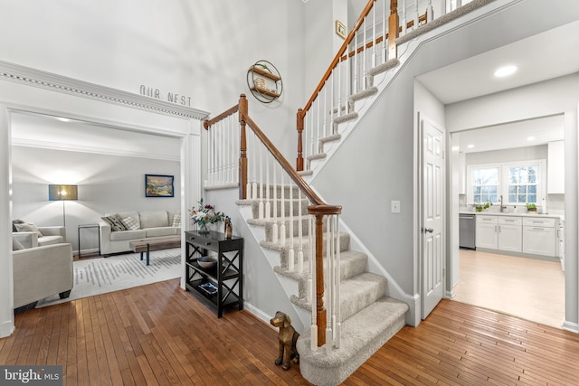 staircase with a high ceiling, recessed lighting, hardwood / wood-style flooring, and baseboards