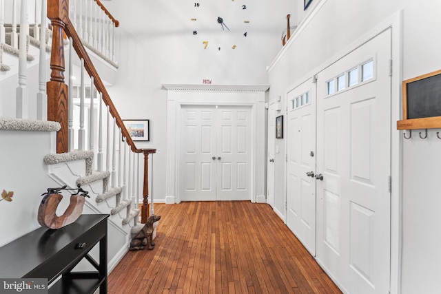 entryway featuring wood-type flooring, baseboards, a high ceiling, and stairs