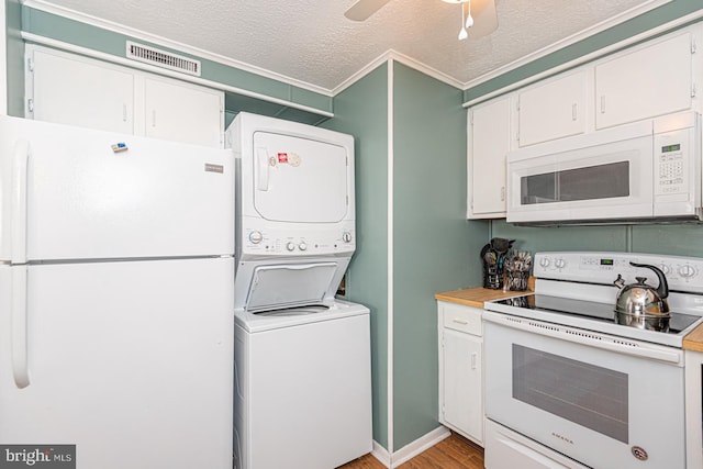 kitchen with white appliances, stacked washer and clothes dryer, a textured ceiling, and white cabinets