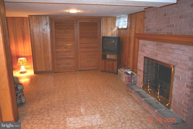 living room featuring a brick fireplace and wood walls