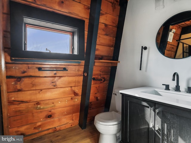 half bathroom featuring vanity, wooden walls, toilet, and wood finished floors