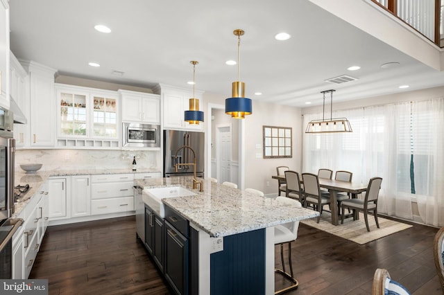 kitchen featuring sink, stainless steel appliances, an island with sink, white cabinets, and decorative light fixtures