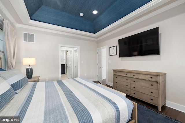 bedroom featuring crown molding, ensuite bath, a raised ceiling, and hardwood / wood-style floors