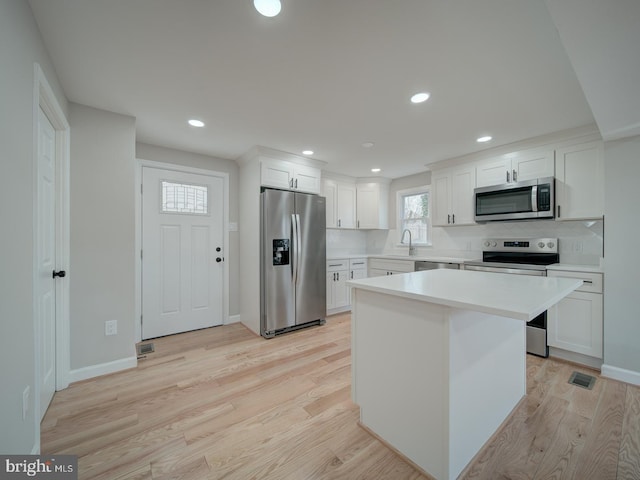 kitchen featuring a kitchen island, tasteful backsplash, white cabinets, stainless steel appliances, and light hardwood / wood-style flooring