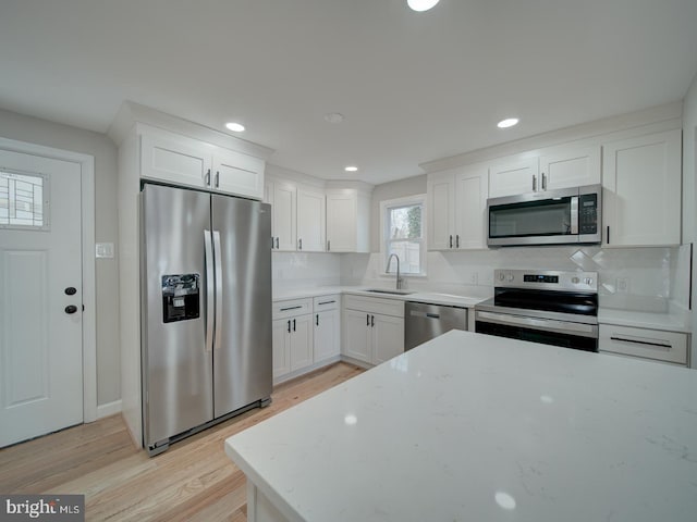 kitchen with appliances with stainless steel finishes, white cabinetry, sink, light stone counters, and light hardwood / wood-style flooring