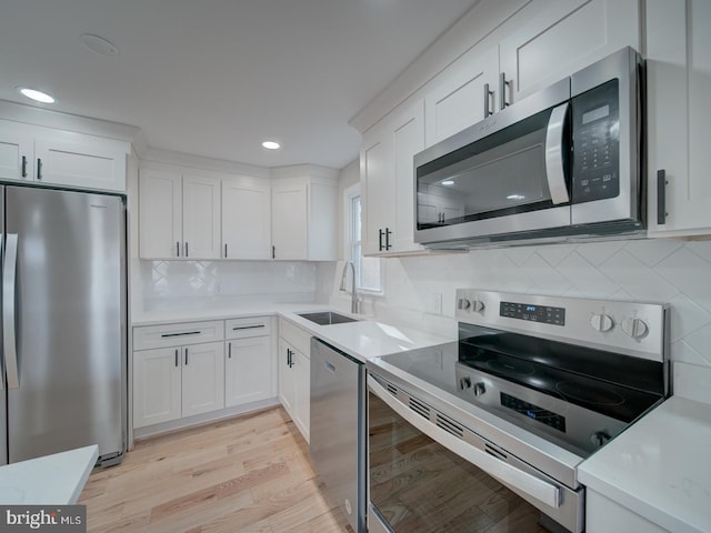 kitchen with appliances with stainless steel finishes, sink, backsplash, white cabinets, and light wood-type flooring