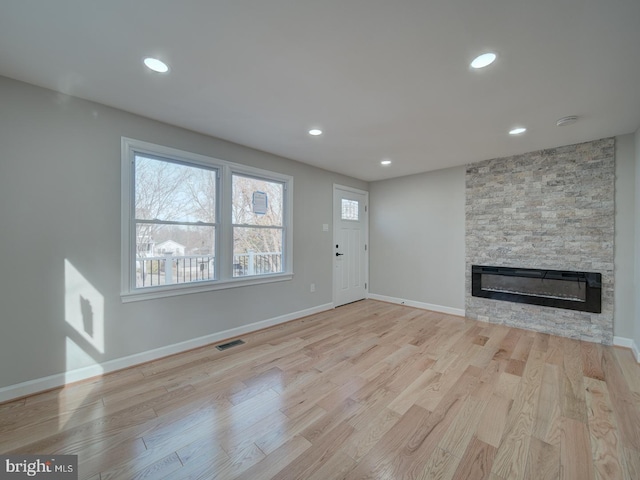 unfurnished living room featuring a stone fireplace and light wood-type flooring