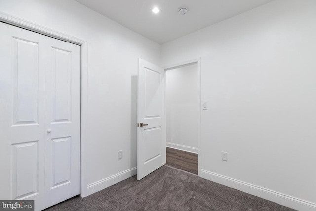 unfurnished bedroom with dark colored carpet and a closet