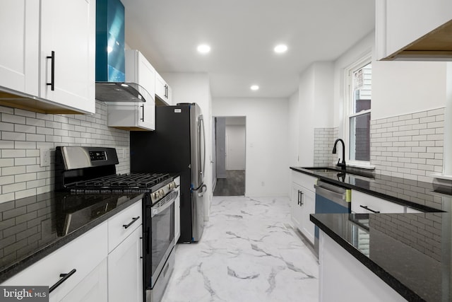 kitchen featuring sink, appliances with stainless steel finishes, white cabinets, dark stone counters, and wall chimney exhaust hood