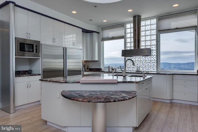 kitchen featuring white cabinetry, built in appliances, a center island with sink, and a wealth of natural light