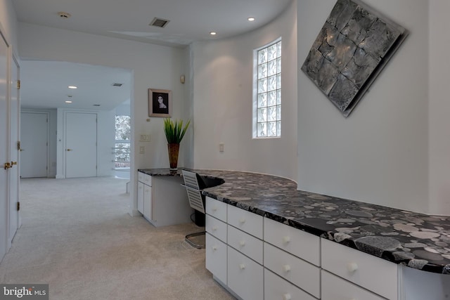 kitchen featuring light carpet, built in desk, dark stone counters, and white cabinets