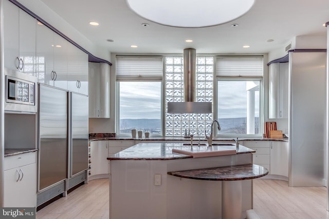 kitchen with sink, white cabinets, a kitchen island with sink, built in appliances, and light wood-type flooring