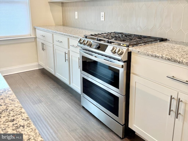 kitchen featuring dark wood-type flooring, light stone counters, white cabinetry, double oven range, and backsplash