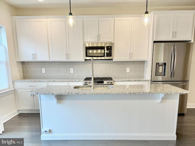 kitchen featuring appliances with stainless steel finishes, pendant lighting, white cabinets, a kitchen island with sink, and light stone counters