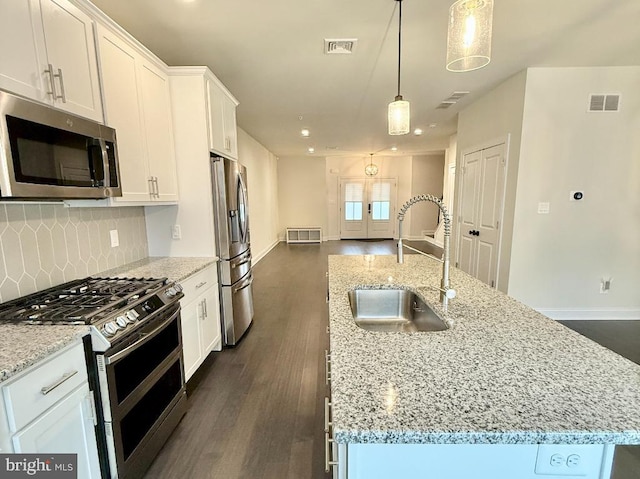 kitchen with sink, hanging light fixtures, an island with sink, stainless steel appliances, and white cabinets