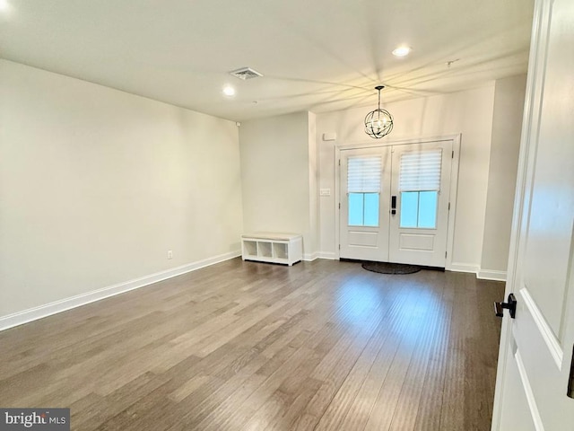 foyer featuring wood-type flooring, an inviting chandelier, and french doors