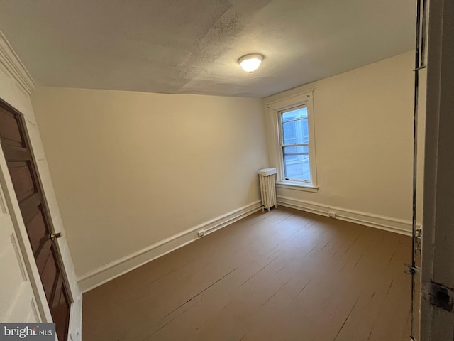 spare room with dark wood-type flooring, radiator, and baseboards