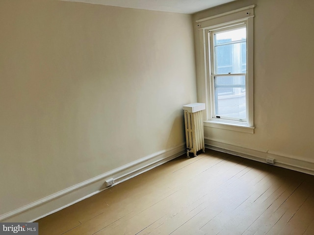 spare room featuring light wood-type flooring, radiator heating unit, and baseboards