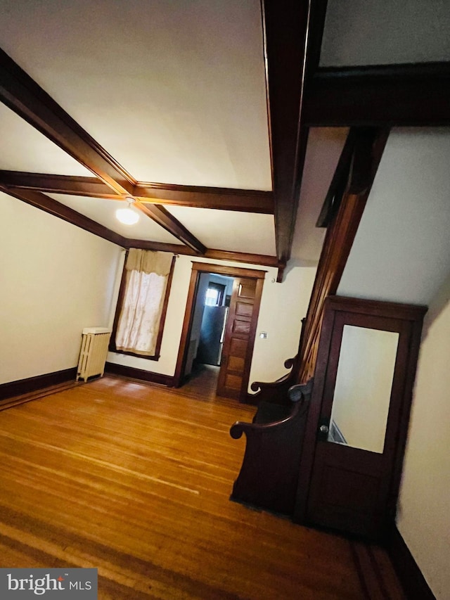 interior space featuring baseboards, beamed ceiling, wood finished floors, and radiator